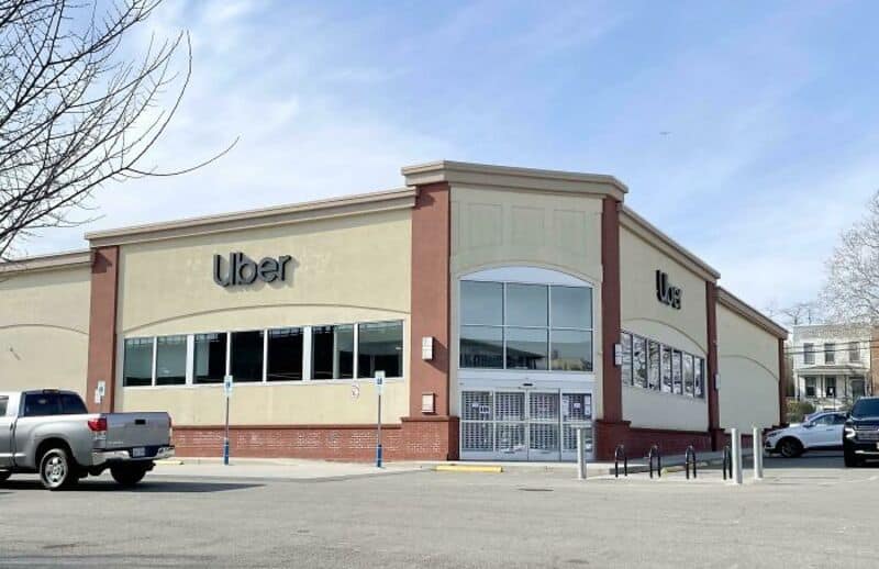Uber building with beige walls, large windows, and a parking lot in front.