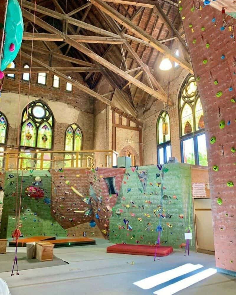 Indoor climbing gym with colorful walls, holds, and wooden ceiling beams.