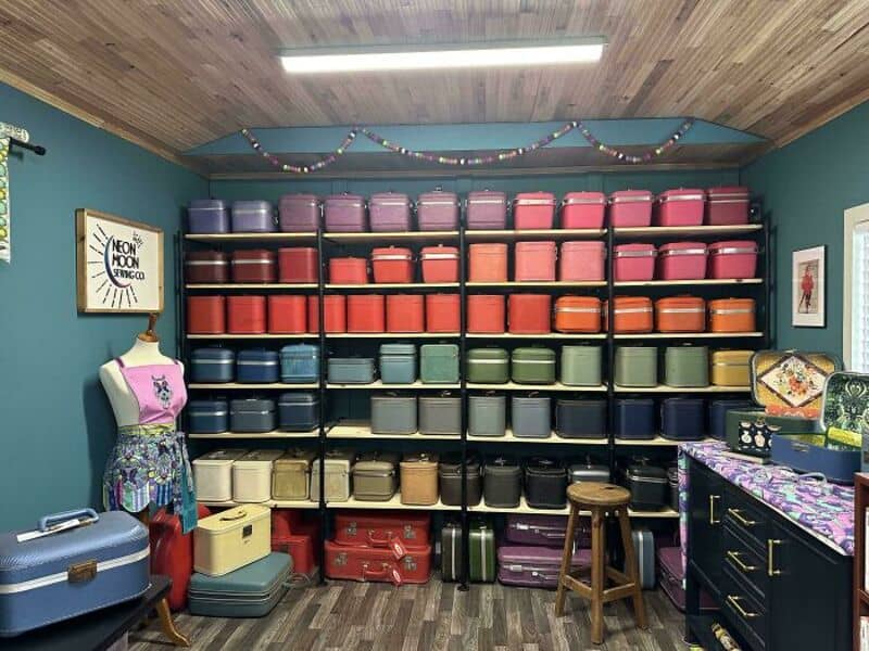Colorful vintage suitcases and trunks on black shelves in a room with teal walls.