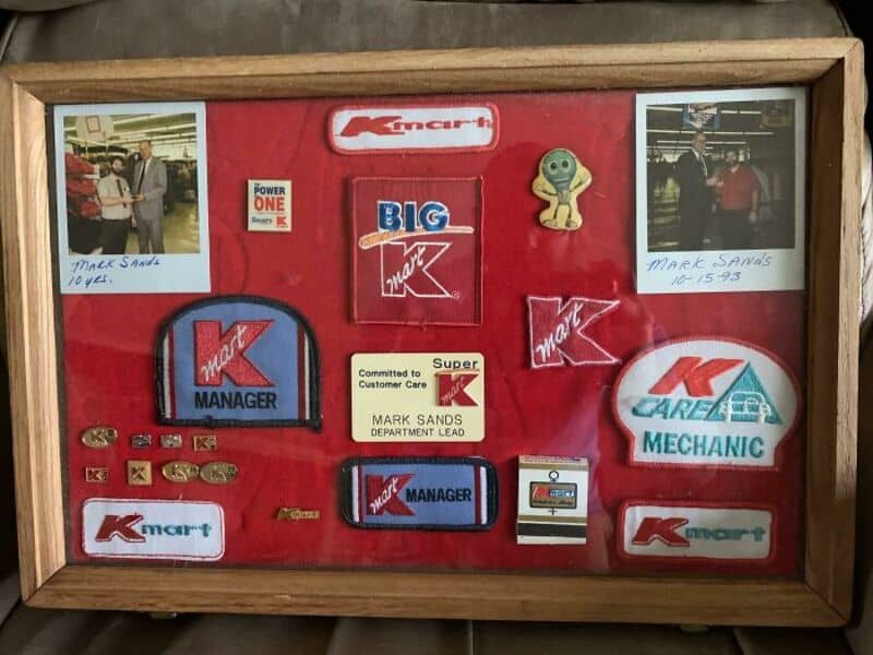 Collection of Kmart memorabilia including patches, badges, and photos in a wooden frame.