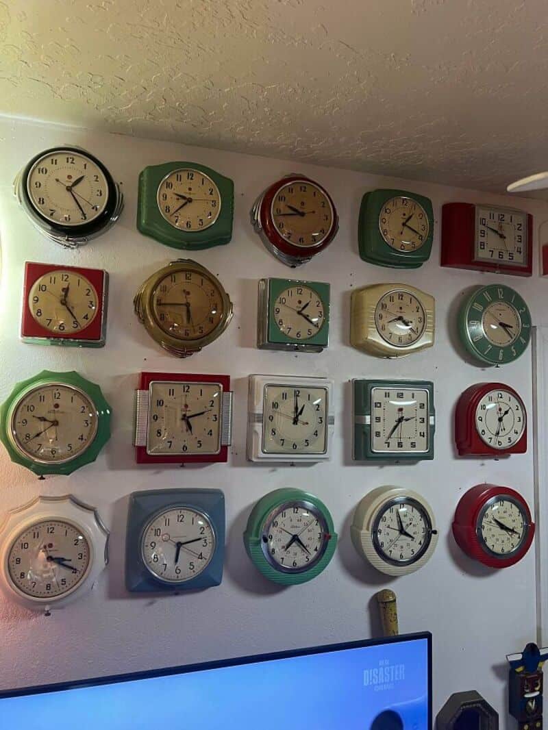 Collection of various wall clocks in different shapes and colors on a white wall.