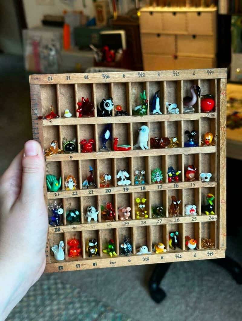 Hand holding a wooden box with small colorful figurines and numbered compartments.