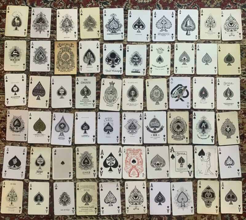 Collection of playing cards with various intricate designs, mostly spades, arranged on a surface.