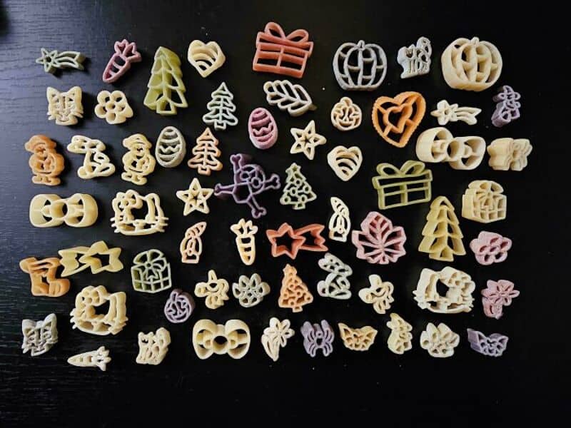 Colorful pasta shapes including pumpkins, hearts, stars, and gifts on black background.