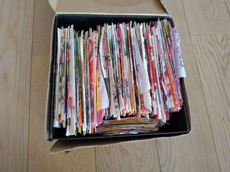 Box of colorful, organized paper with tabs and labels on a wooden floor.