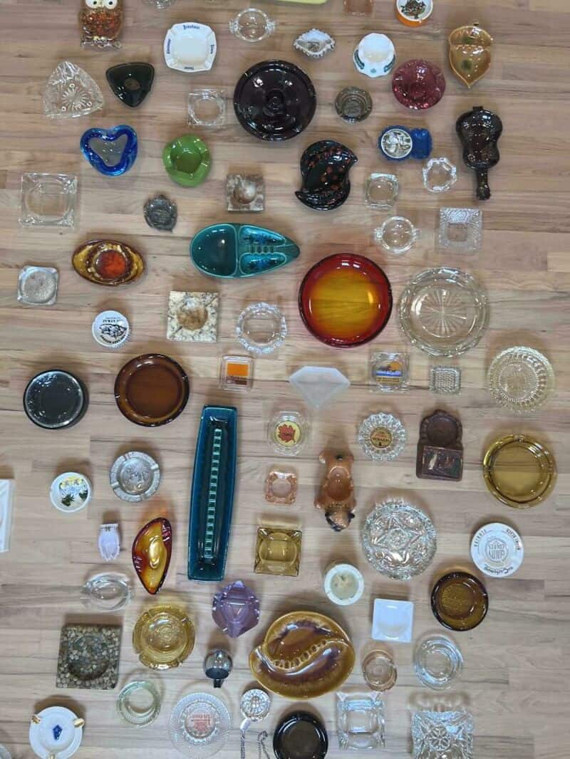 Collection of various glass and ceramic items on wooden floor, including bowls, vases, and figurines.