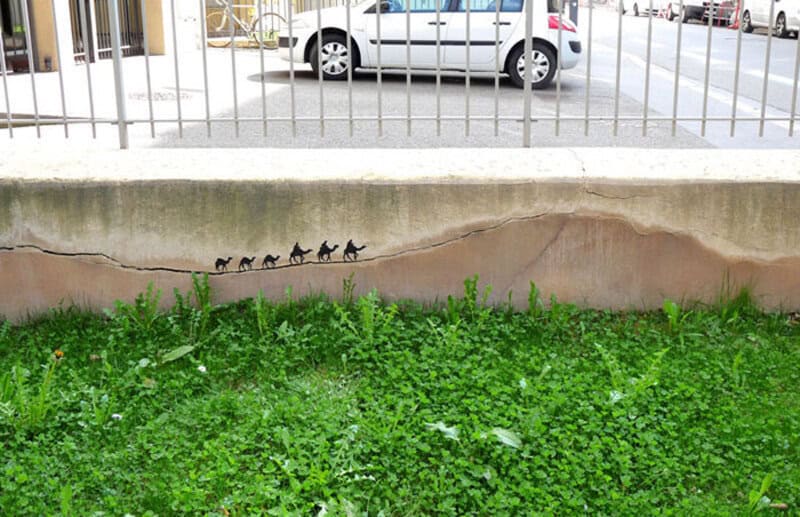 Cats painted on wall with green grass below and a white fence above.