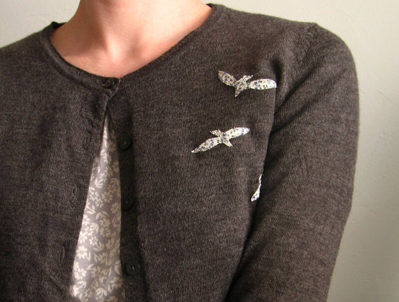 Close-up of a woman wearing a dark cardigan with butterfly pins.