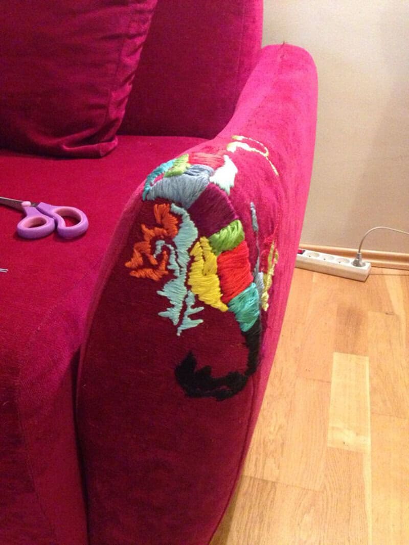 Colorful embroidered patch on a red sofa armrest with scissors nearby.