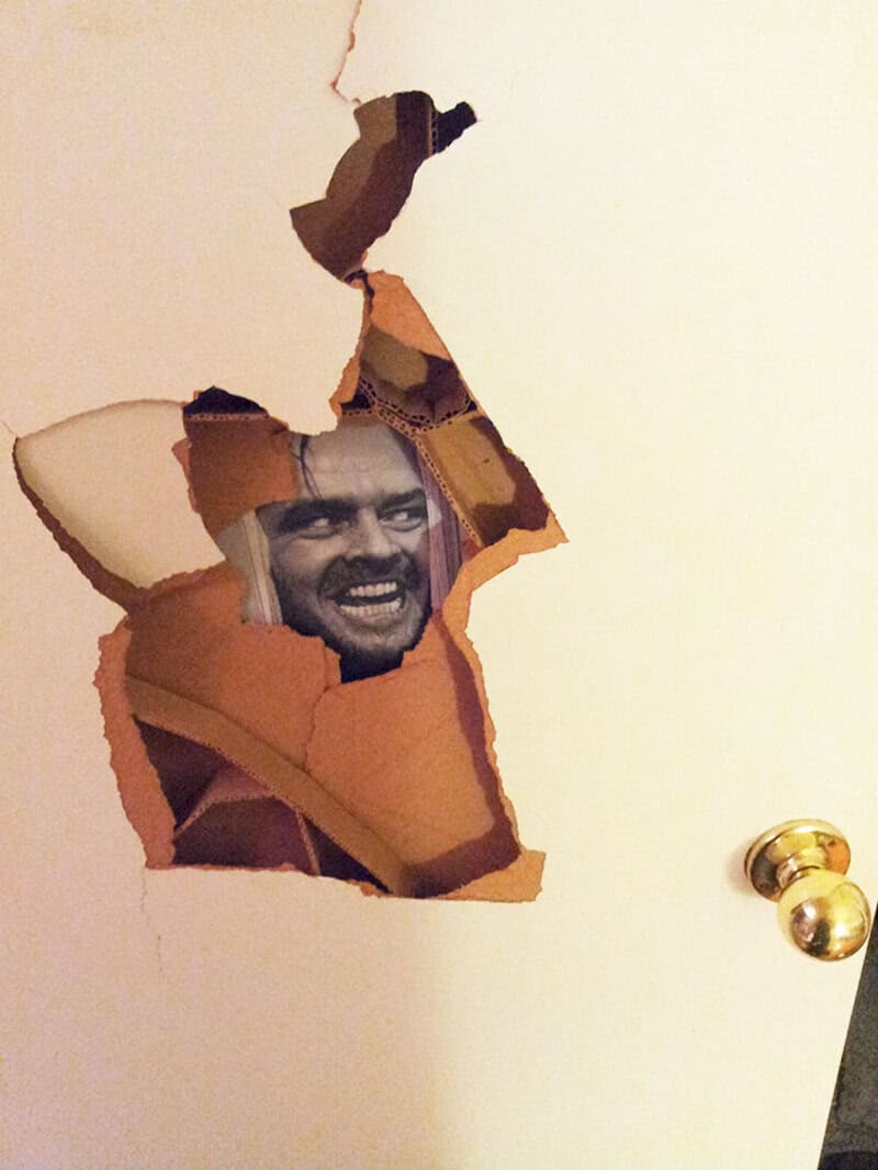 Person smiling behind a torn hole in a door.