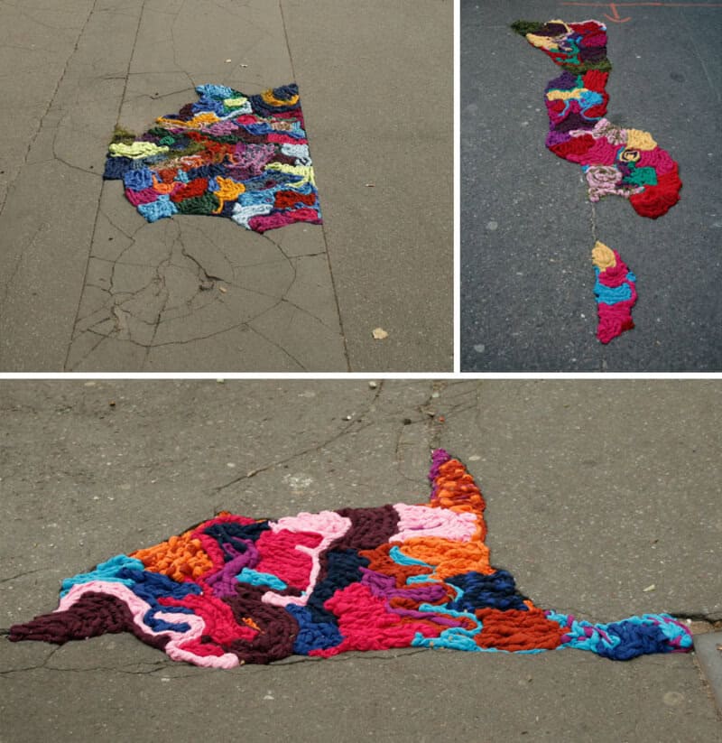 Colorful yarn art pieces on cracked pavement, resembling maps and abstract shapes.