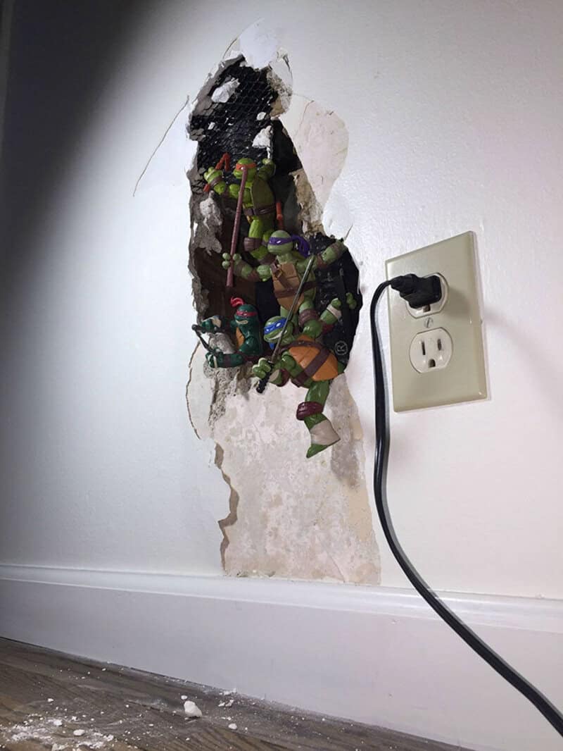Broken wall with a power outlet and a plug, toys inside the hole.
