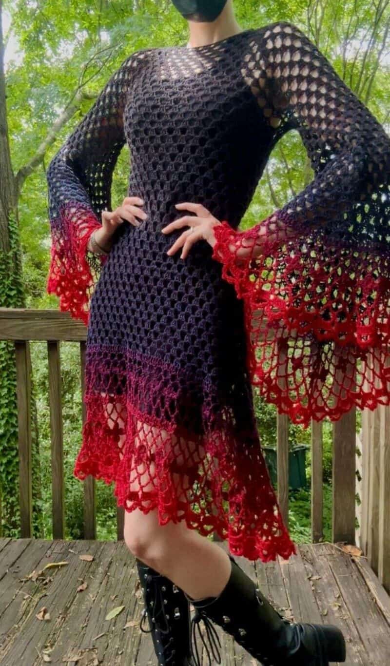 Woman in black crochet dress with red accents, standing outdoors on a wooden deck.