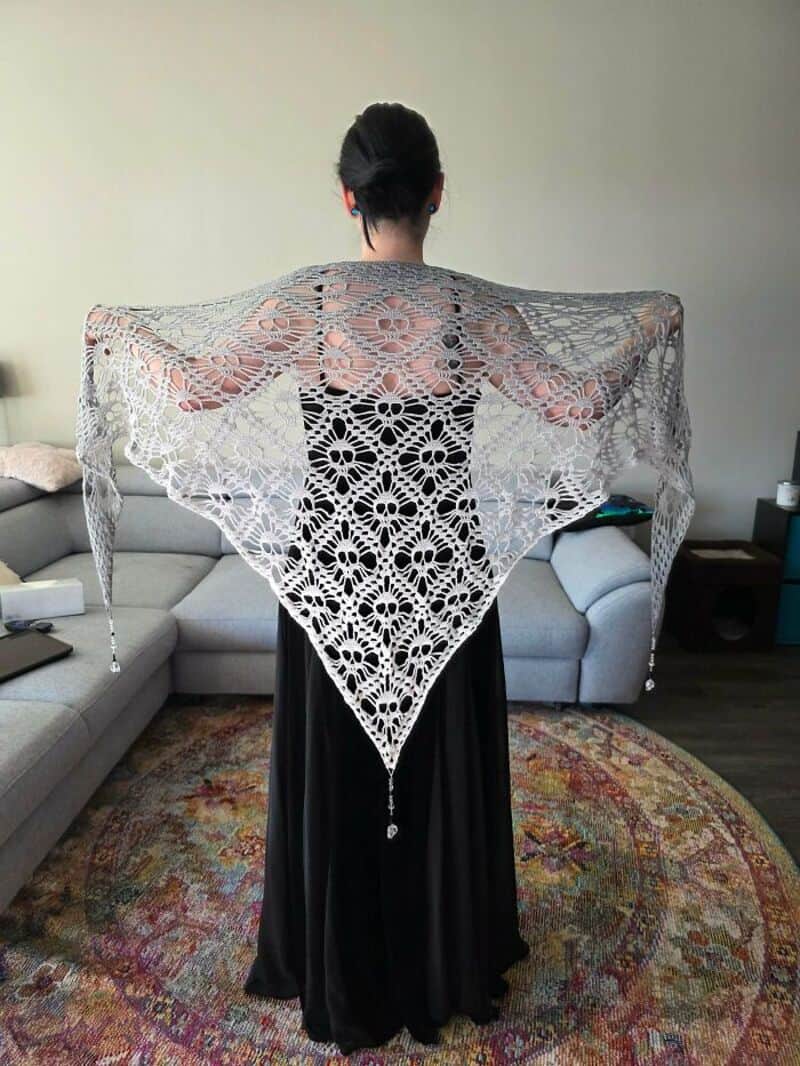 Woman with a black dress and a large, intricate crochet shawl in a living room.