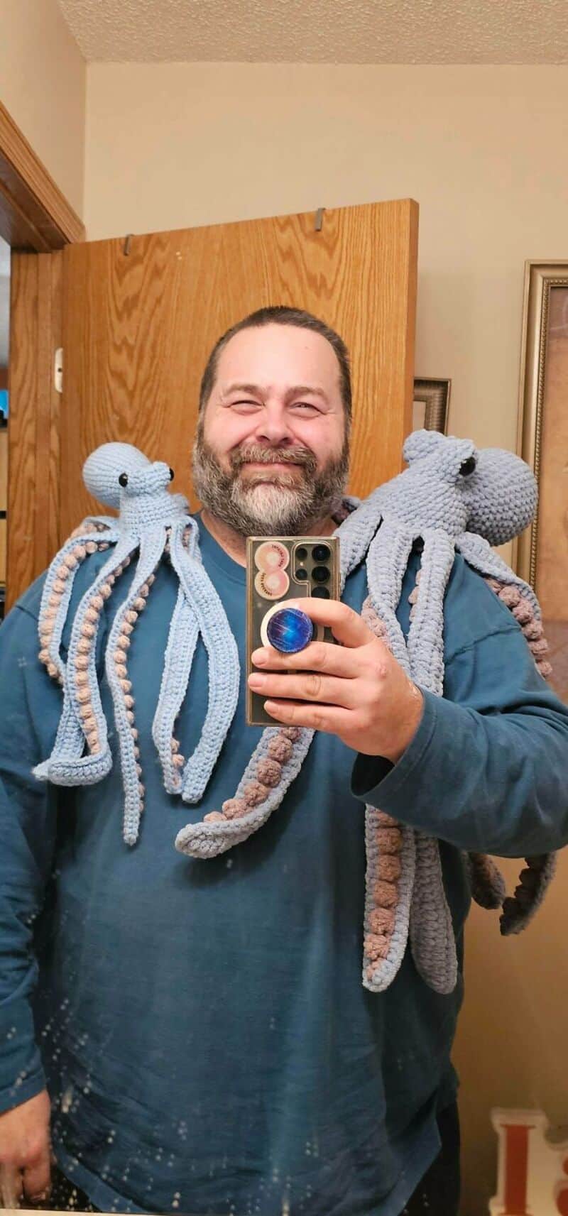 Man with a beard taking a selfie with crochet octopus toys on his shoulders.