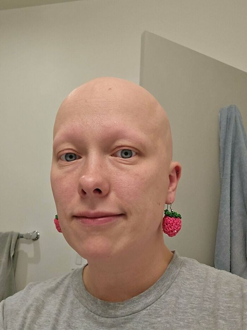 Person with a bald head wearing strawberry-shaped earrings in a bathroom.