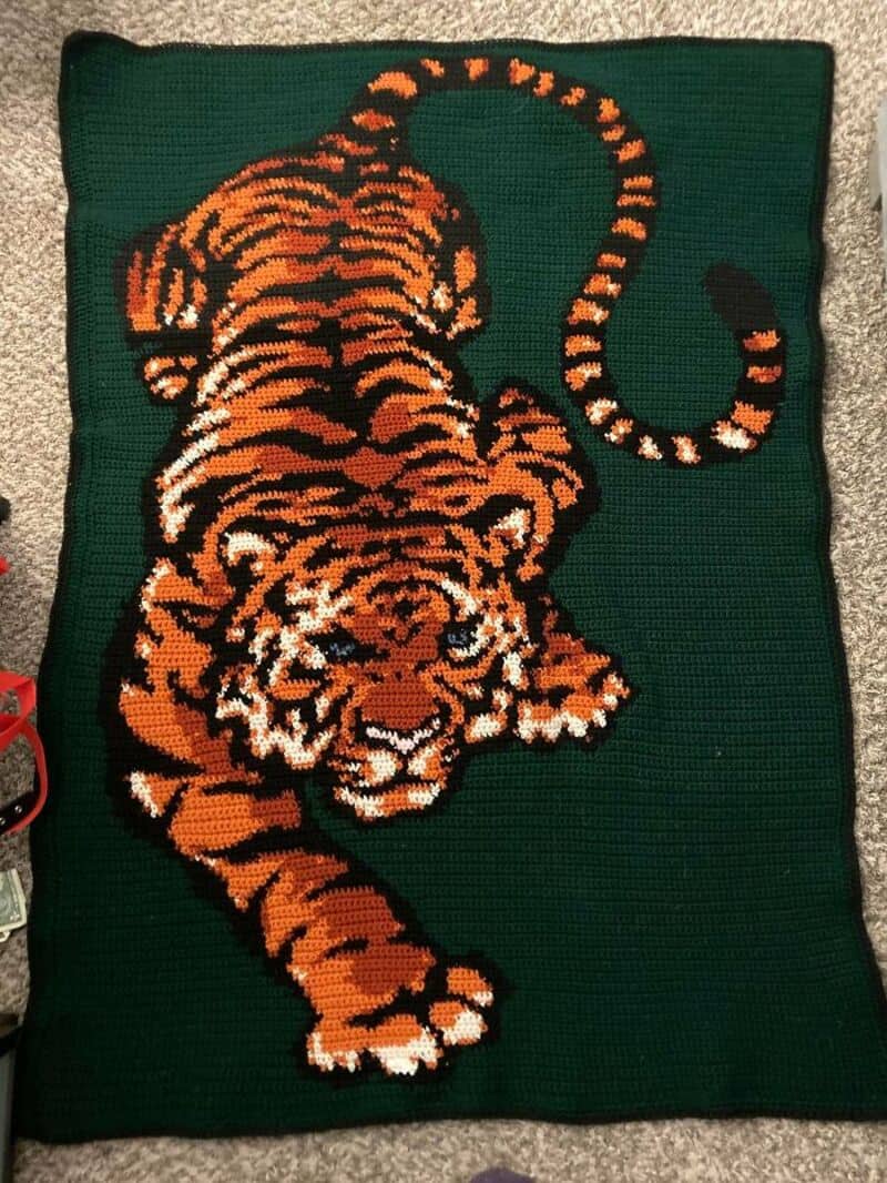 Crochet tiger rug with orange, black, and white details on a green background.