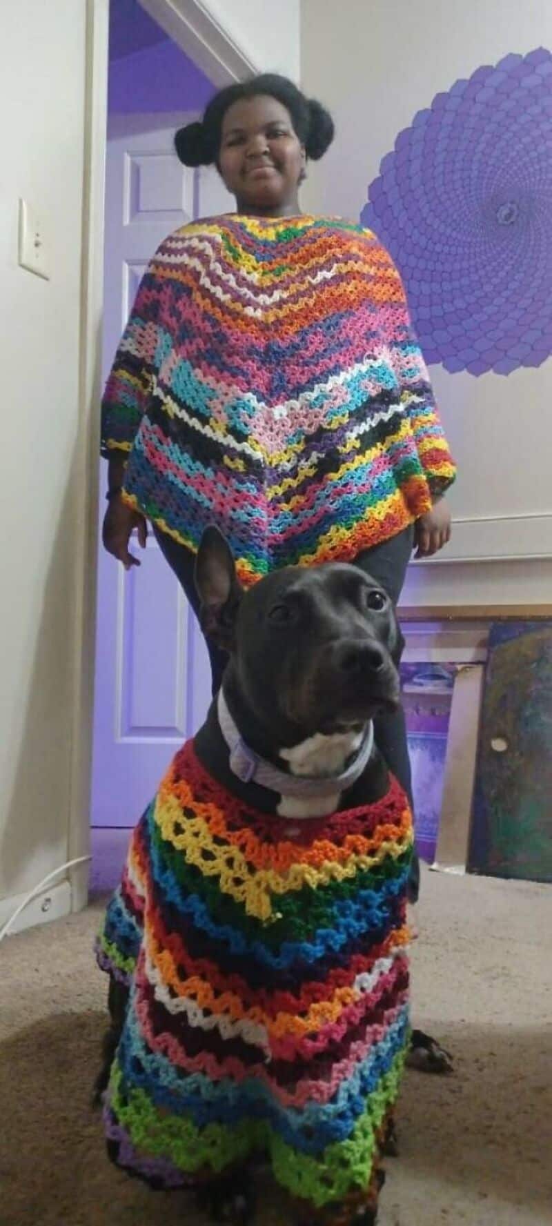 Girl and dog wearing colorful crochet outfits in a room.