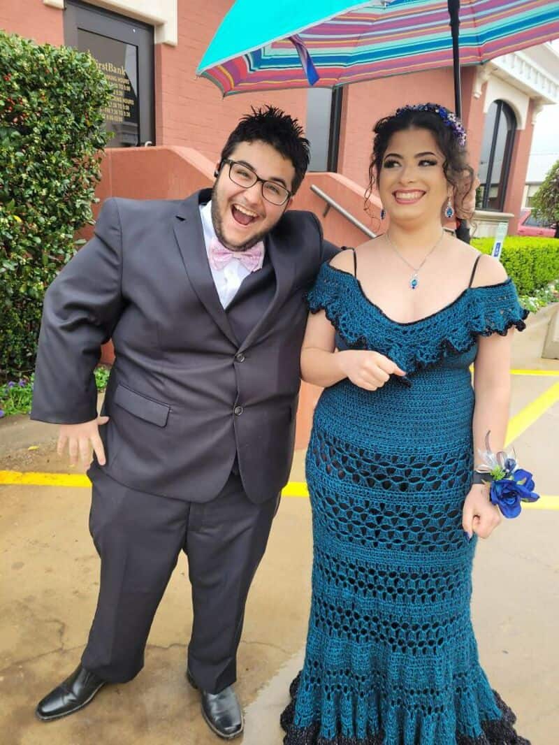 Happy couple in formal attire under a colorful umbrella outside.