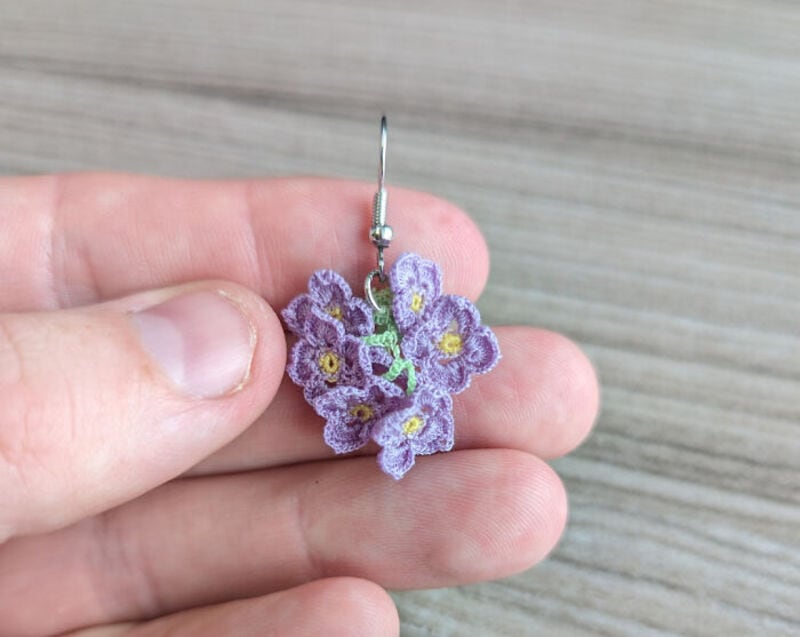 Hand holding a crochet flower earring with purple flowers and yellow centers.