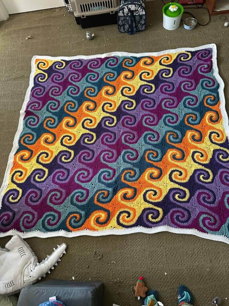 Colorful crochet blanket with swirling patterns in purple, yellow, orange, and teal.