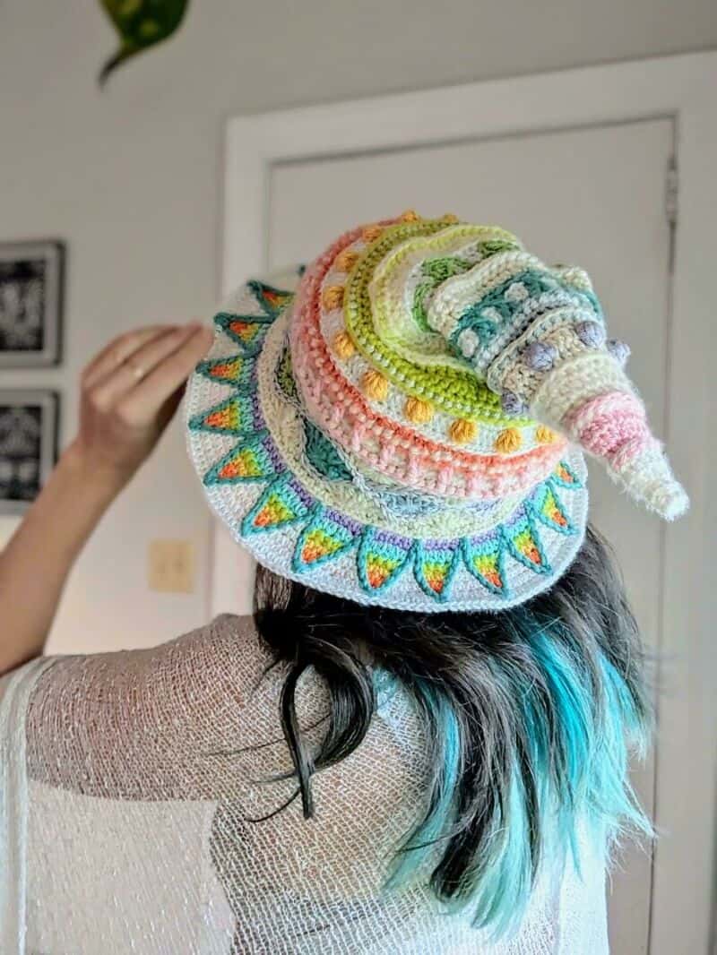 Colorful crochet hat with a spiral design and a wide brim, worn by a person with black and blue hair.