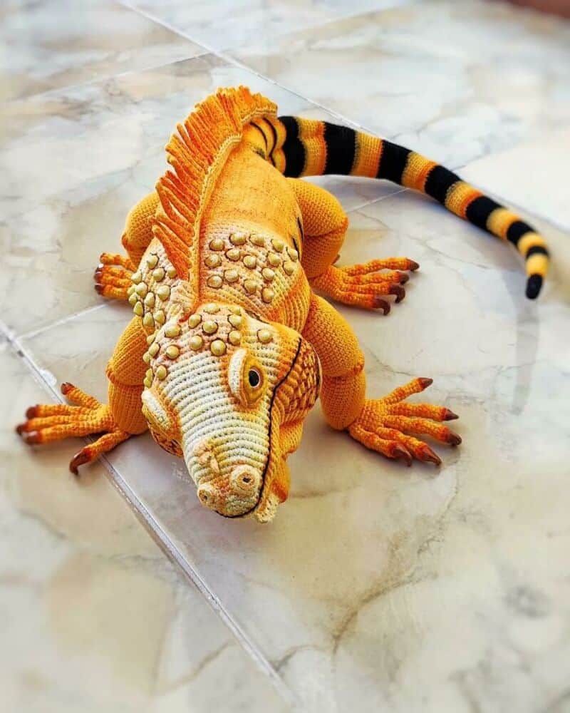 Yellow and orange plush iguana with a striped tail on a marble floor.