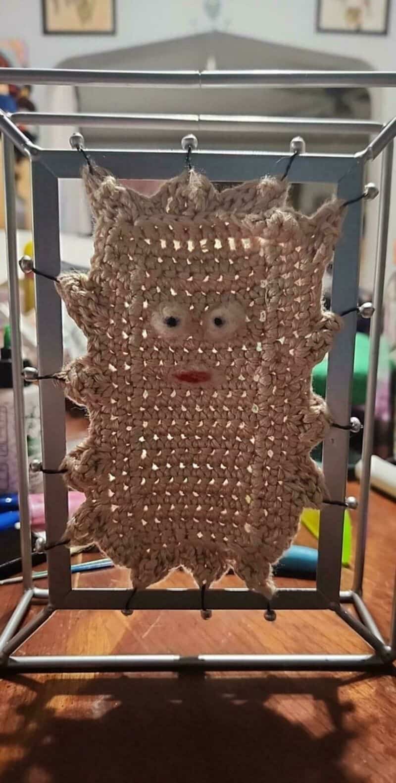 Crocheted face with ears, eyes, nose, and mouth on a beige background.