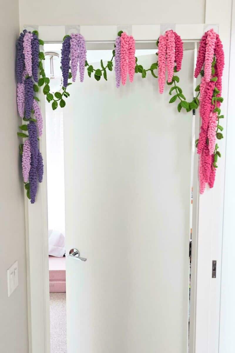 Colorful crochet flowers and green leaves hanging on a white door frame.
