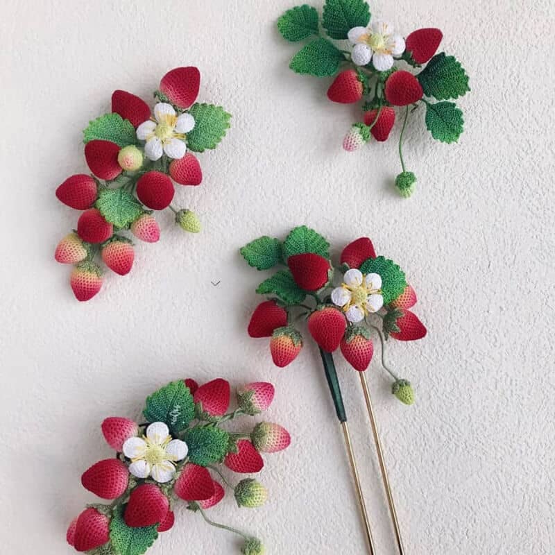 Crochet strawberry and flower decorations on a white wall.