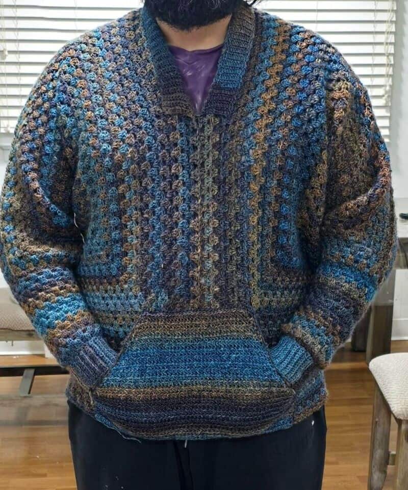 Close-up of a multicolored crochet sweater worn by a person with hands in pockets.