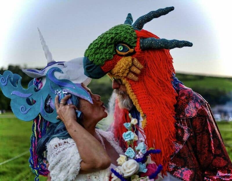 Two people in colorful, fantasy creature costumes face each other outdoors.