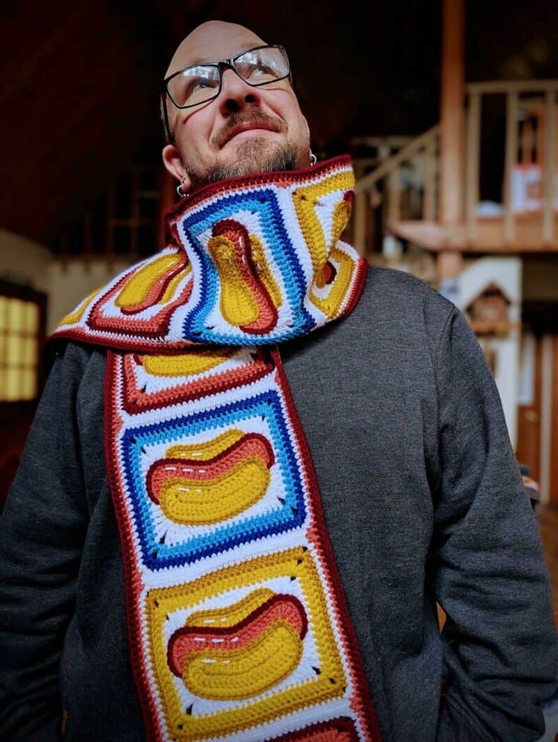 Man wearing a colorful crochet scarf with yellow, red, and blue patterns.