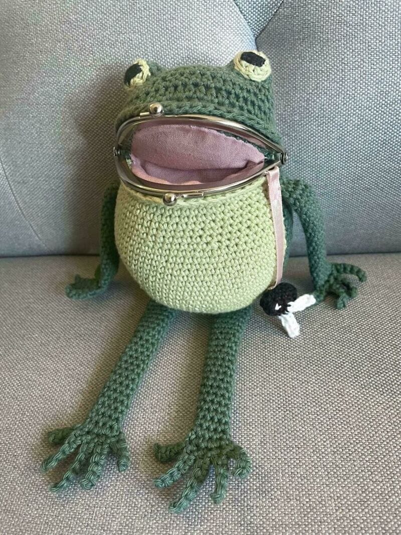Crochet frog coin purse with limbs and eyes, sitting on a gray surface.