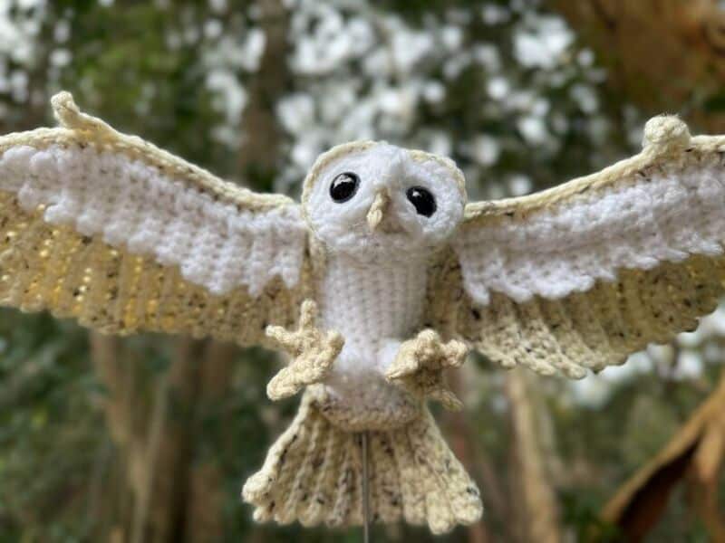 Crocheted owl with outstretched wings hanging outdoors.