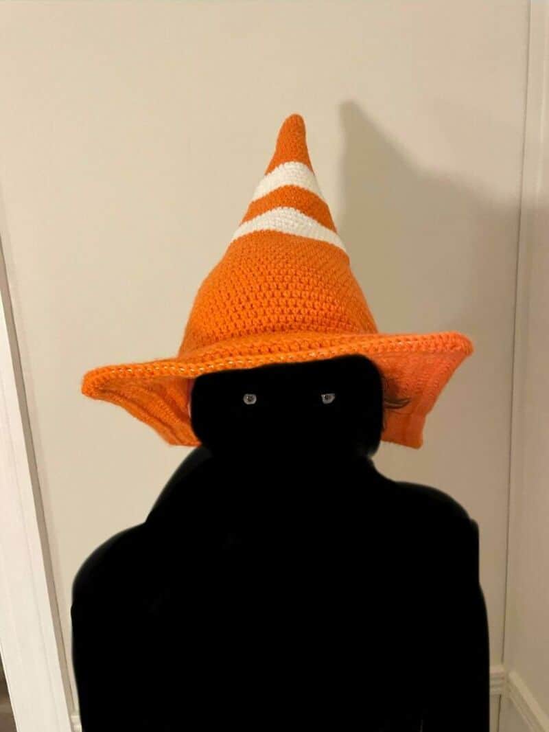 Person wearing a black outfit with an orange and white striped crochet hat.
