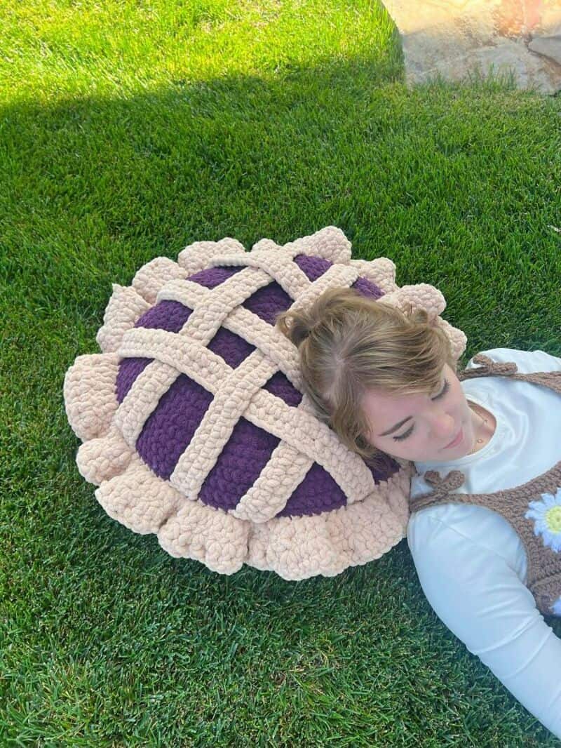 Girl lying on grass with a large purple and beige crochet pillow.