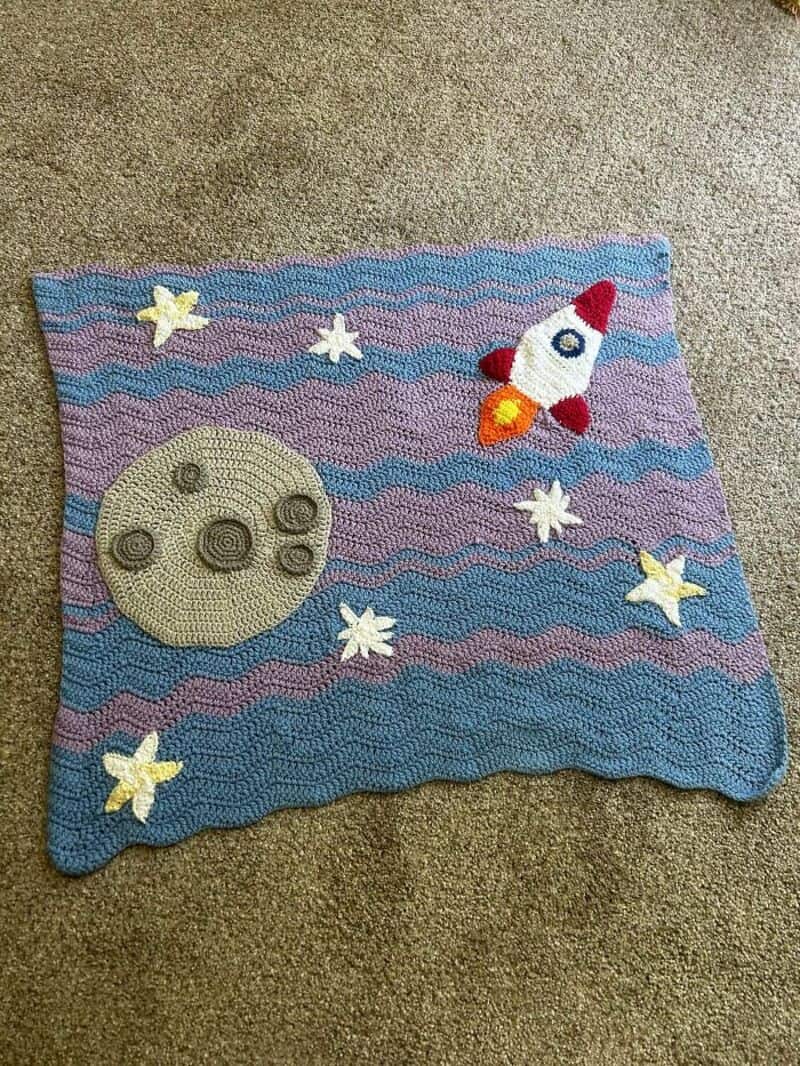 Crochet space-themed rug with moon, stars, and rocket ship design.
