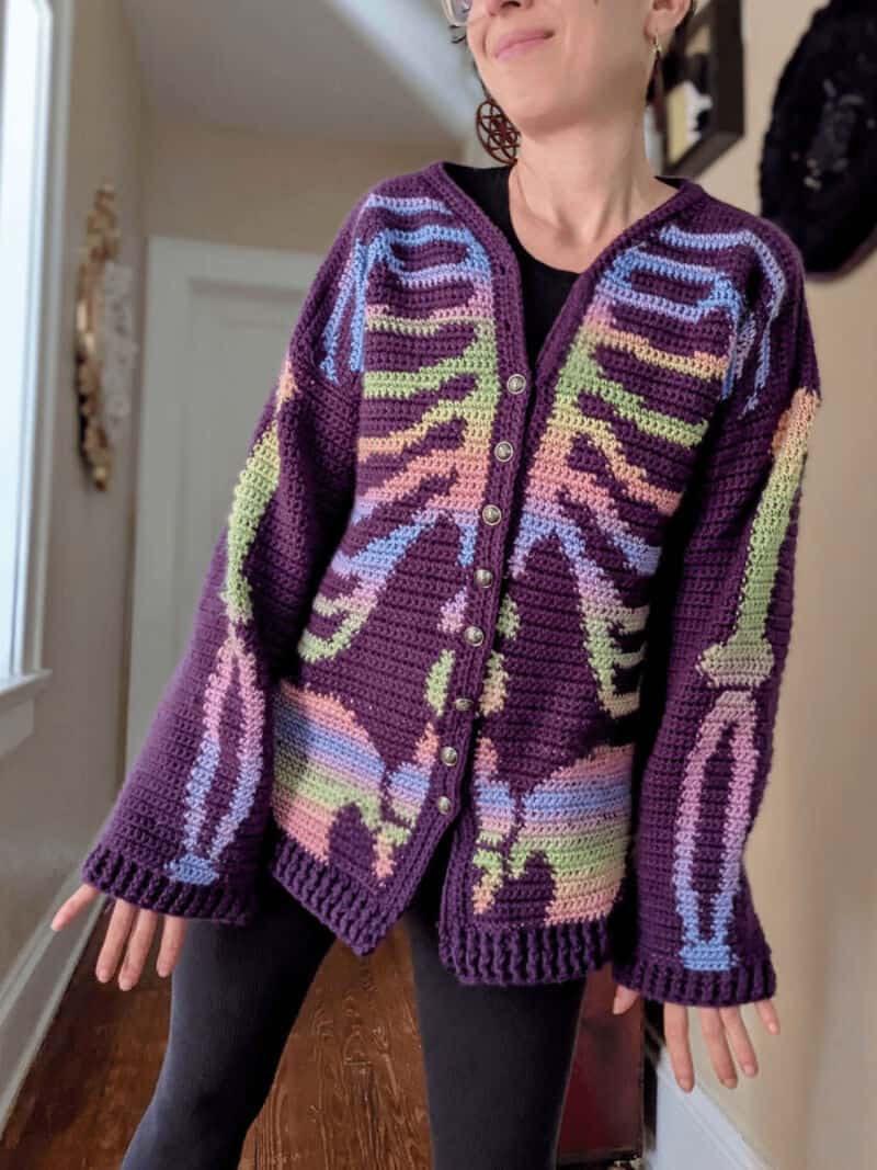 Colorful crochet cardigan with purple, green, and blue patterns, worn by a woman.