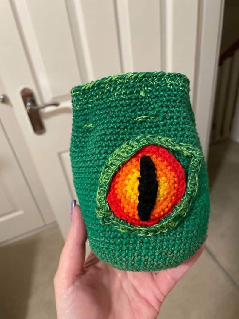 Handmade crochet green monster with a large eye and black slit pupil.