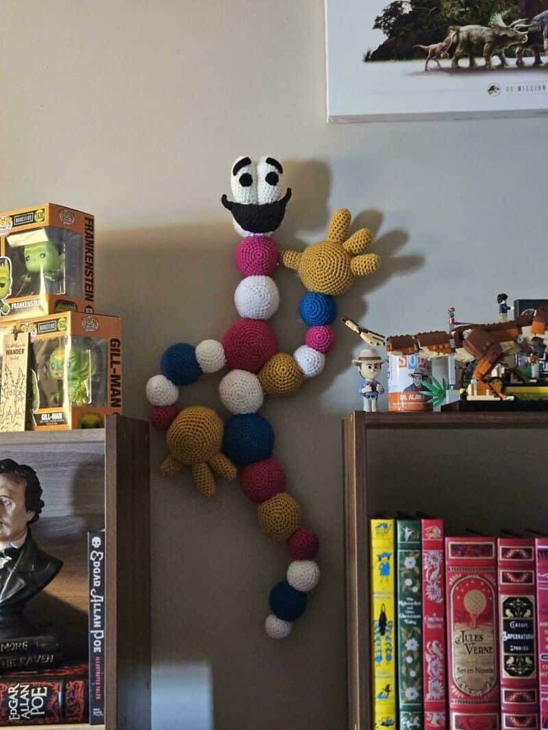 Colorful crochet snake with a smiling face hanging on the wall in a room.