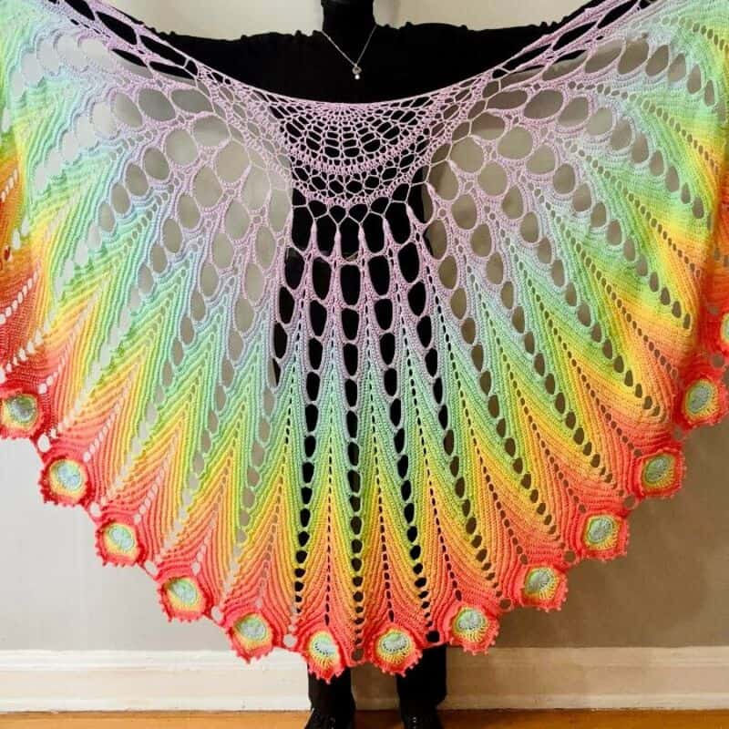 Colorful crochet shawl with rainbow gradient and intricate pattern.