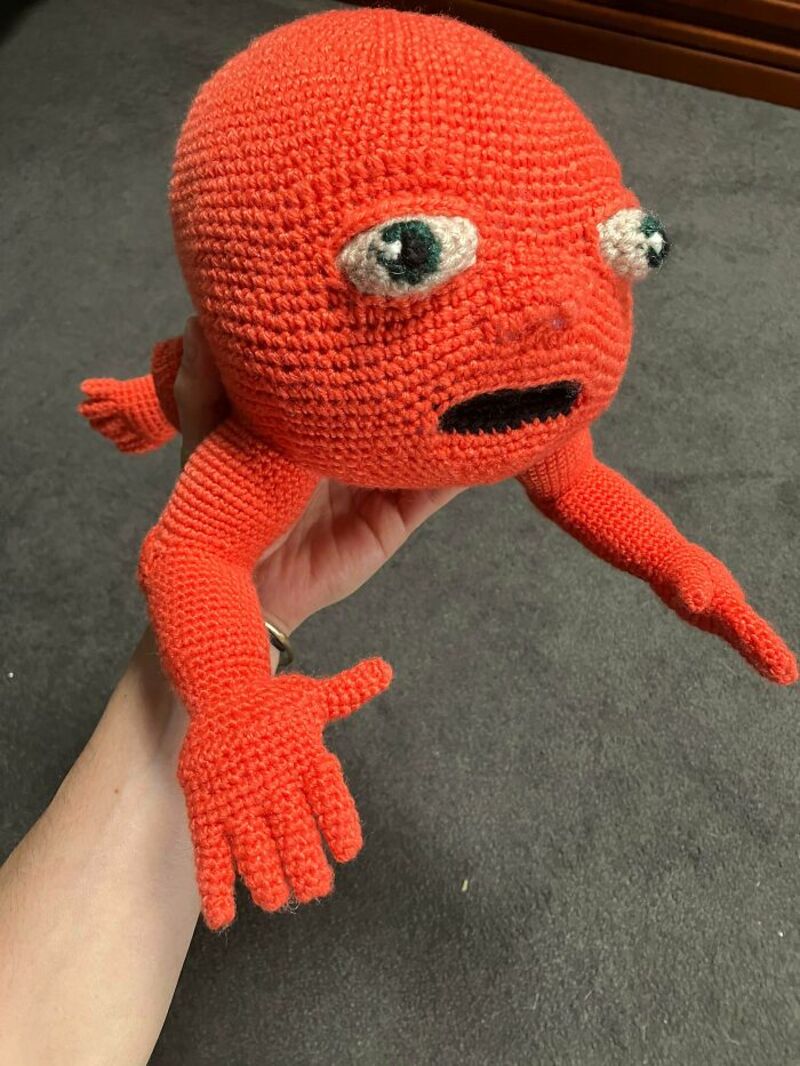 Crochet plush toy resembling a red crab with big eyes and a sad expression.