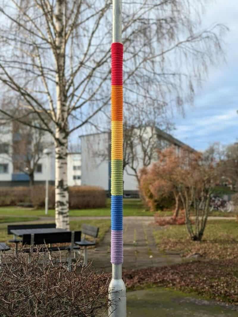 Colorful yarn-wrapped pole in a park with trees and benches.