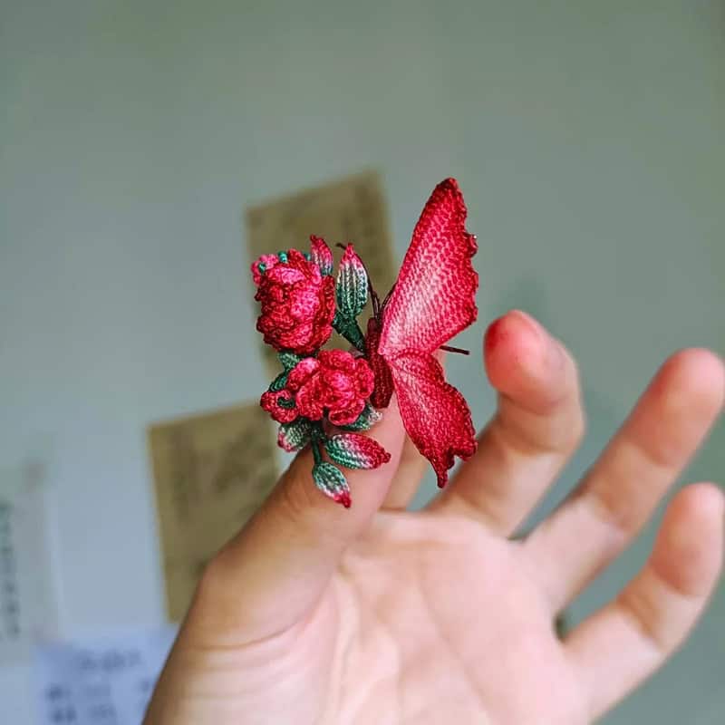 Hand holding a pink embroidered butterfly with flowers on the wing.