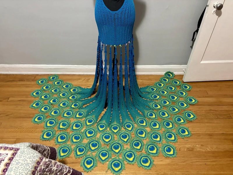 Crochet peacock feather dress with a peacock feather rug on wooden floor.