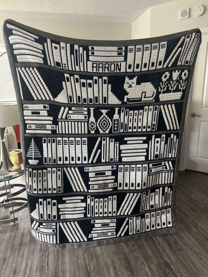 Black and white bookshelf blanket with books, a dog, and a plant design.