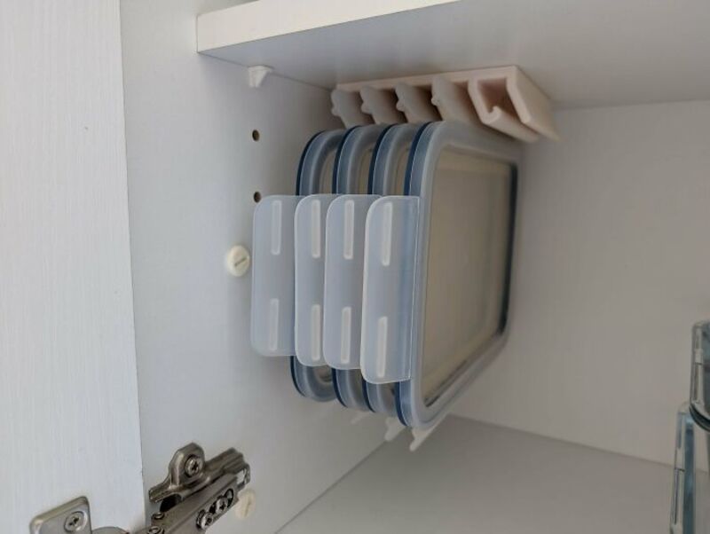 Stacked plastic food storage containers with lids in a cabinet.
