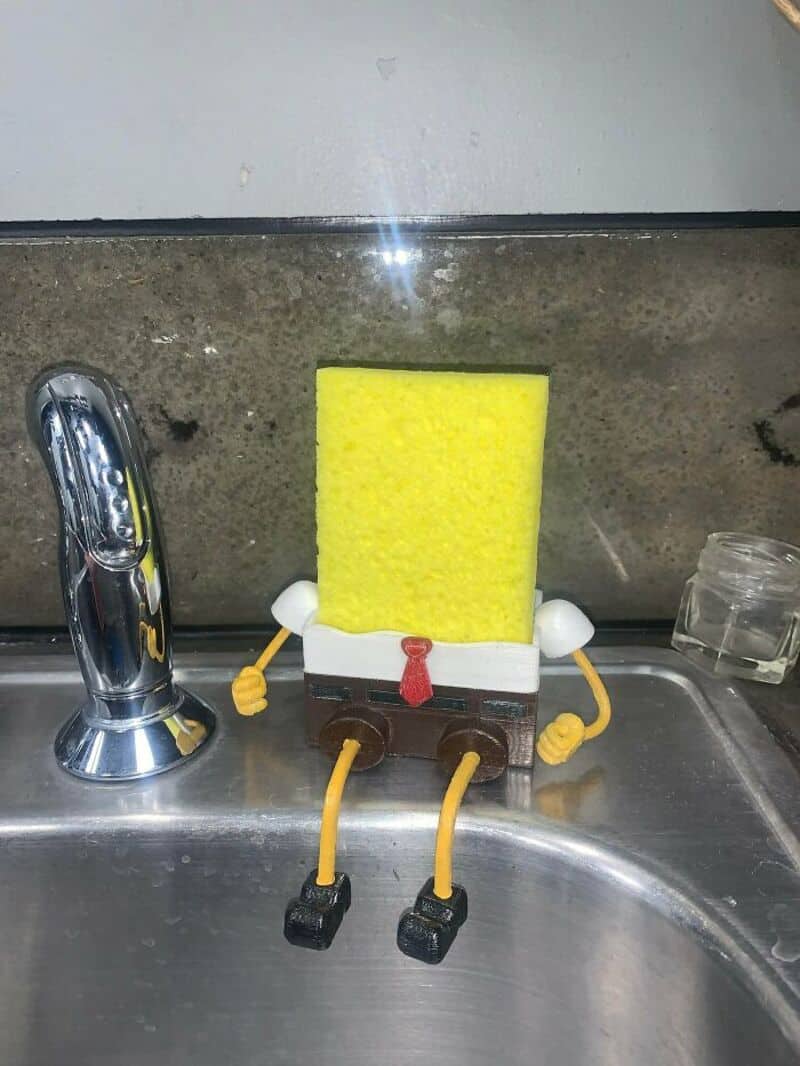 SpongeBob SquarePants figure sitting on a kitchen sink with arms and legs.