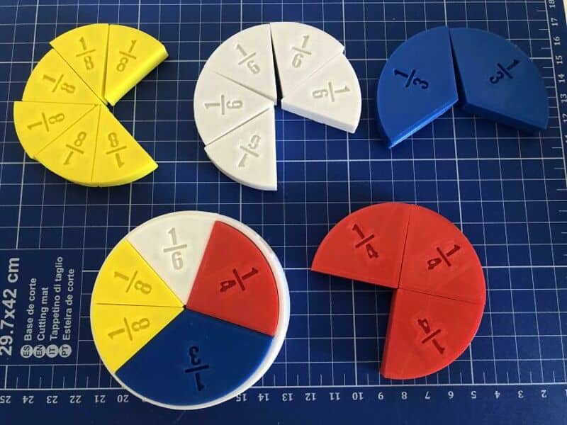 Colorful fraction pie charts on a blue grid cutting mat.